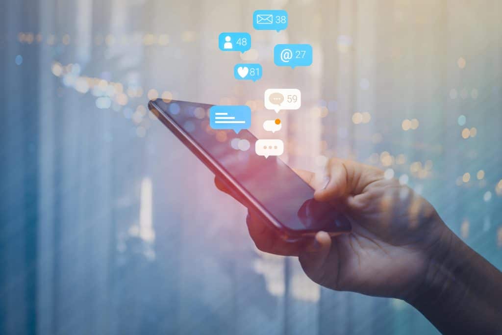 Person holding a phone with icons for messages and likes surrounding it.